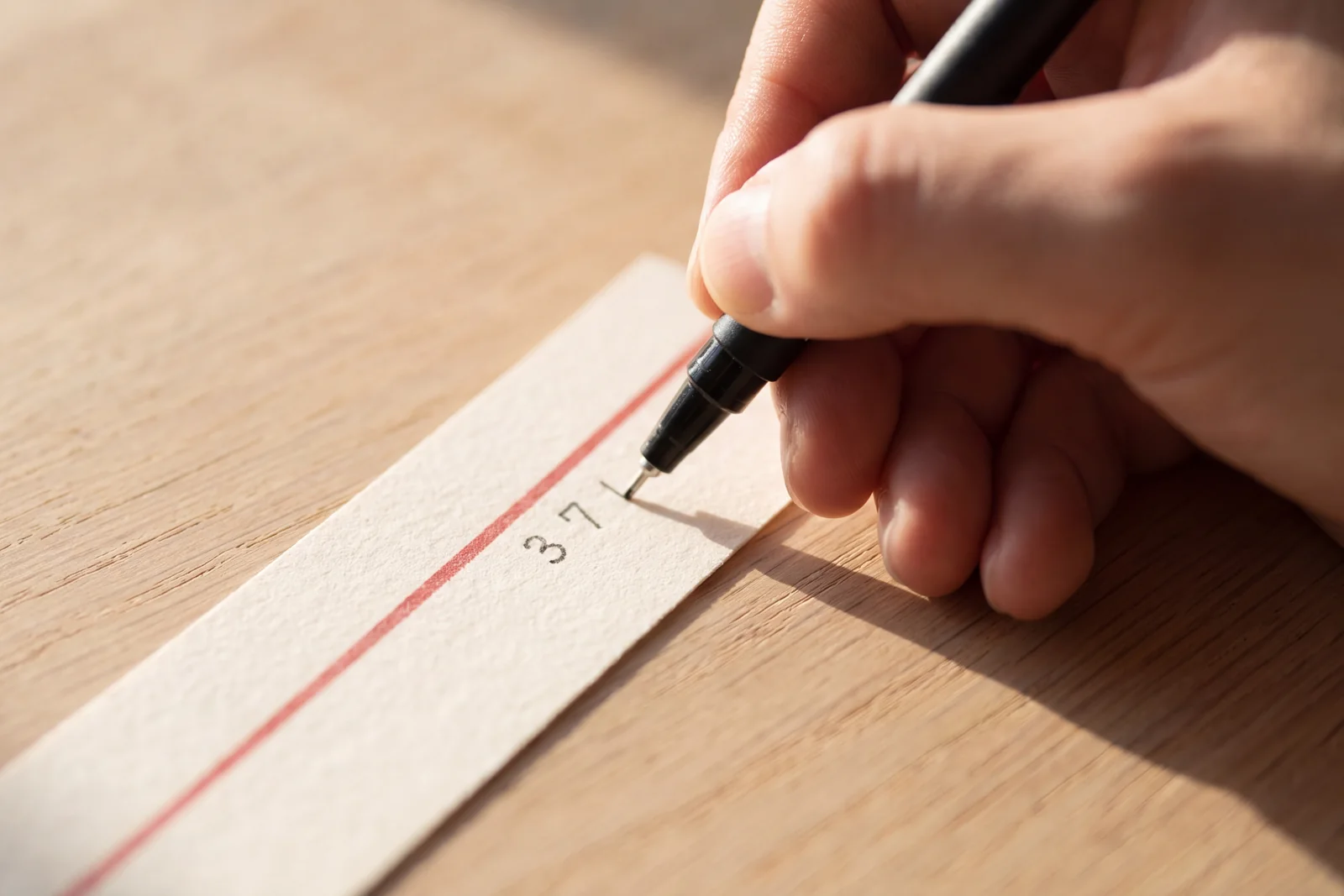 A hand writing a number by hand on a paper band with a red stripe