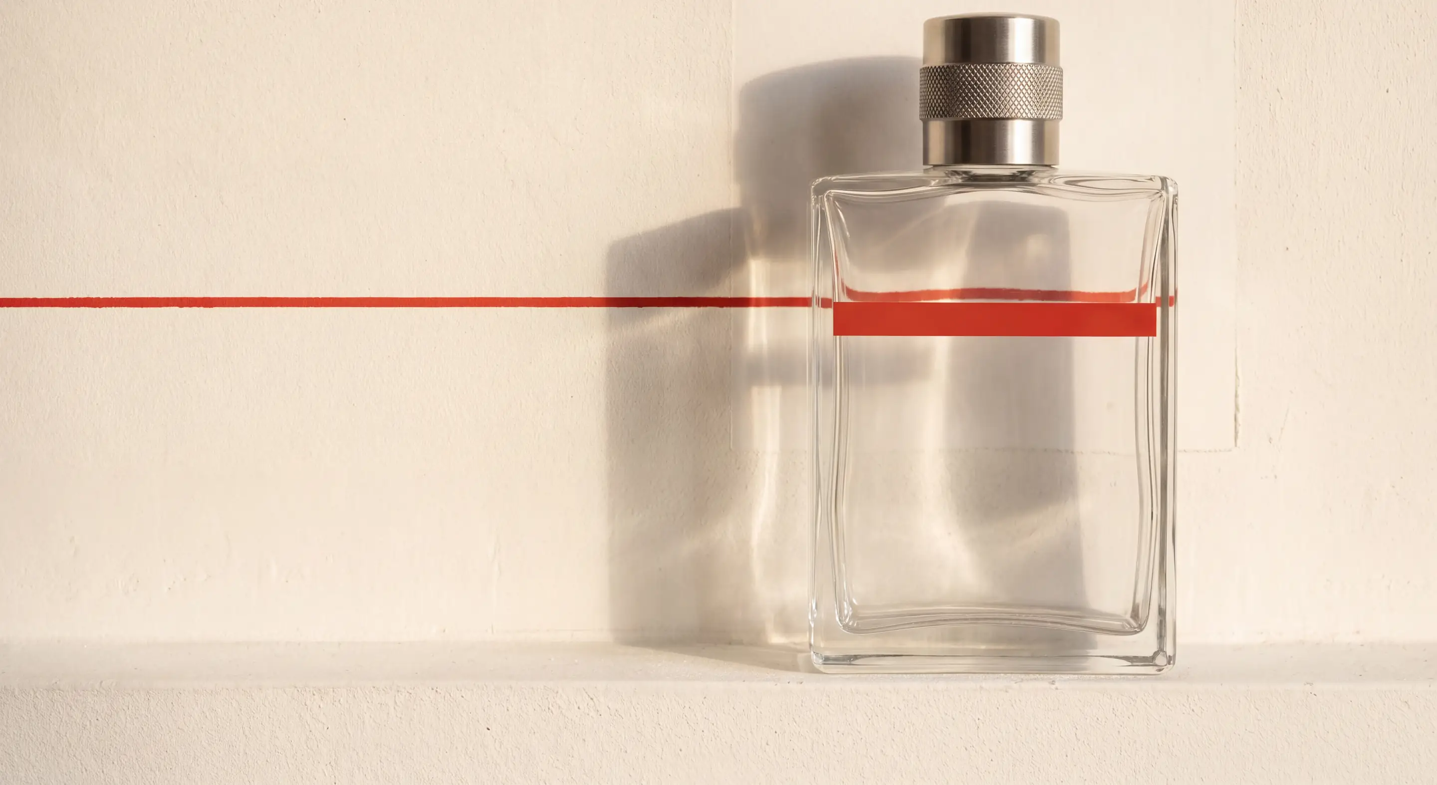 The 50 ml flask on a plaster ledge, a red line painted across the wall behind it meeting the flask&rsquo;s own red band, beside the unfaded rectangle where a picture once hung