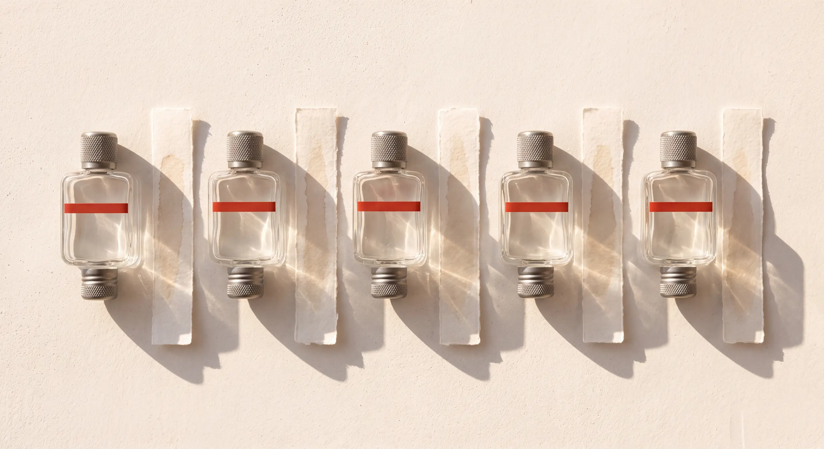 The five flasks seen from above on warm plaster, a paper scent strip laid beside each one