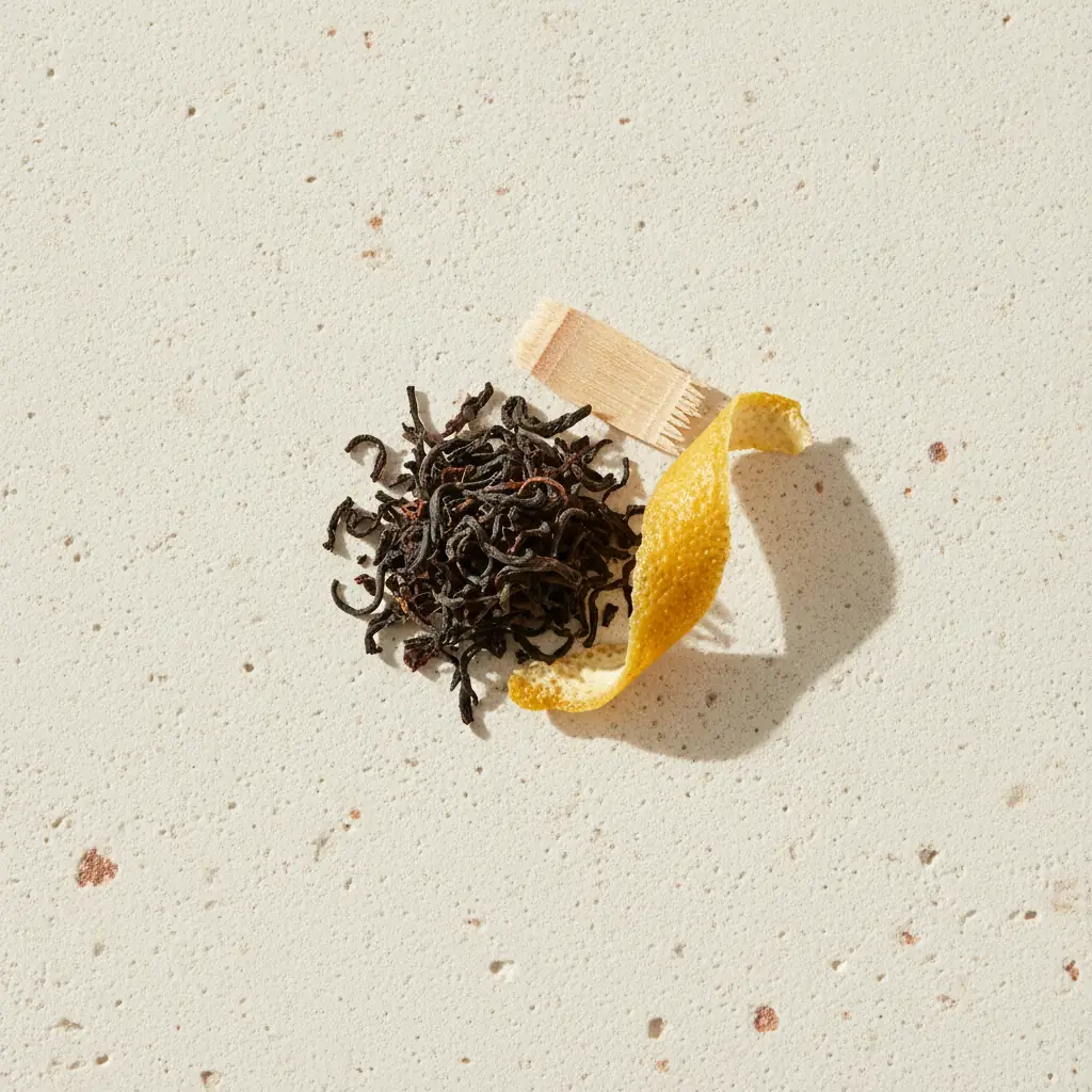 Black tea leaves, a curl of dried lemon peel and pale wood shavings on cream stone